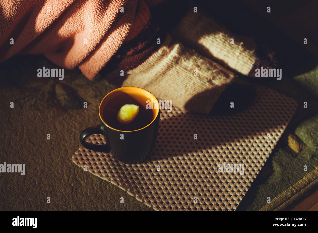 Una tazza di tè caldo con limone e una donna seduta in calzini di lana e una vestaglia spugna, un concetto di riscaldamento autunno Foto Stock