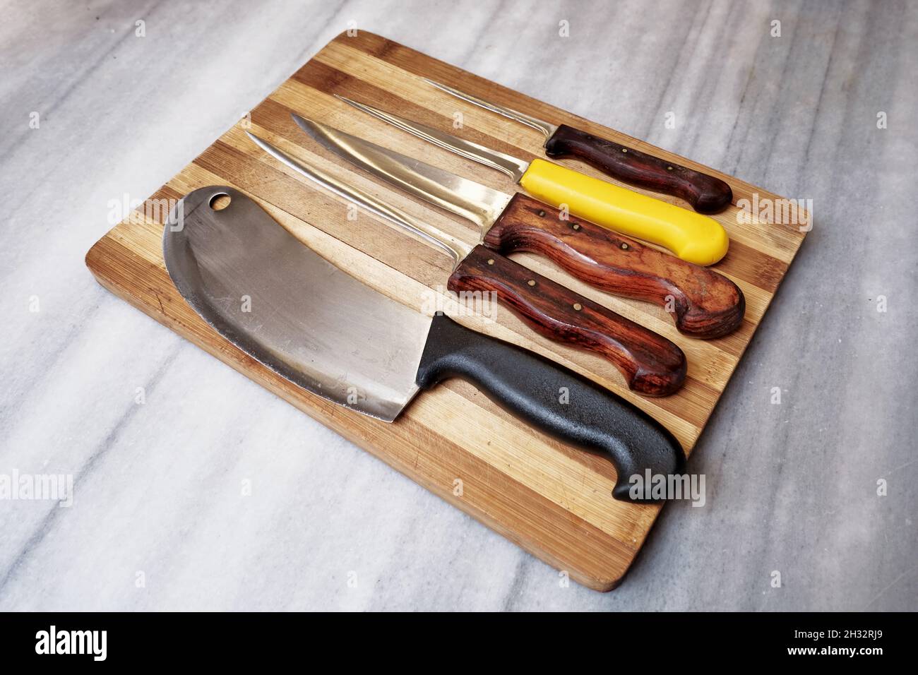Set di coltelli dello chef su un tagliere di legno sul banco da cucina in marmo. Foto Stock