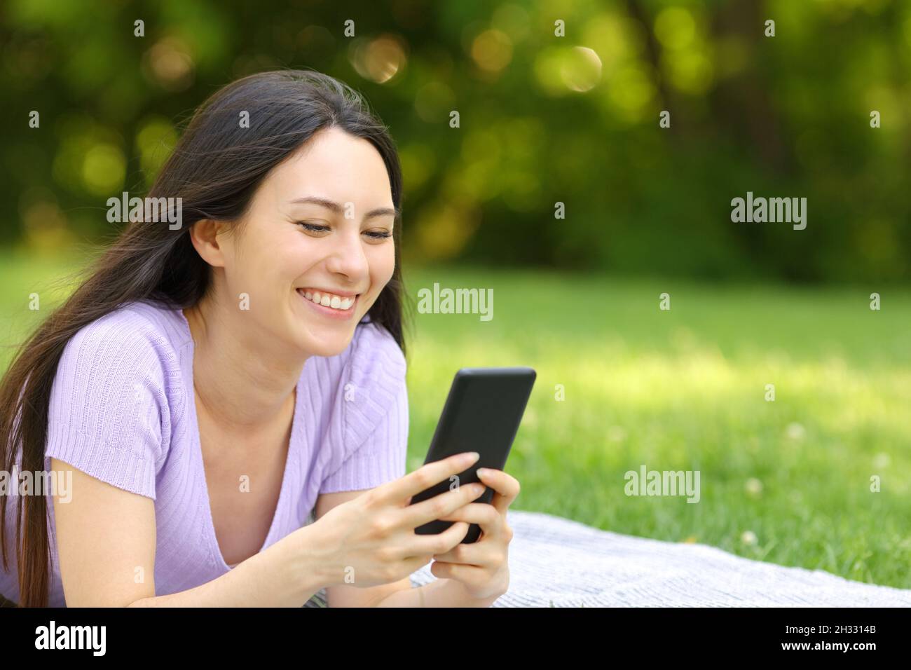 Donna asiatica felice che controlla il telefono cellulare che giace sull'erba in un parco Foto Stock