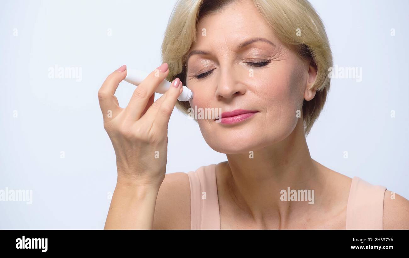 donna matura ad occhi chiusi con rullo in gel antirughe isolato su bianco Foto Stock