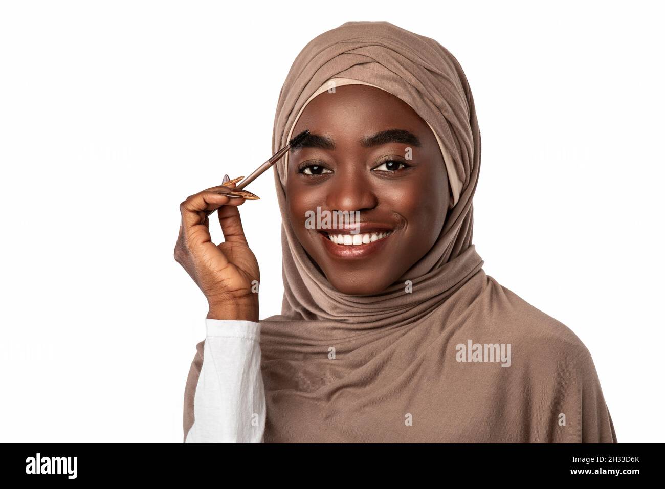 Concetto di trucco naturale. Attraente Happy Muslim Black Lady spazzolare Eyebrow Holding Brush godersi la routine di bellezza del mattino e guardare la fotocamera. Female Foto Stock