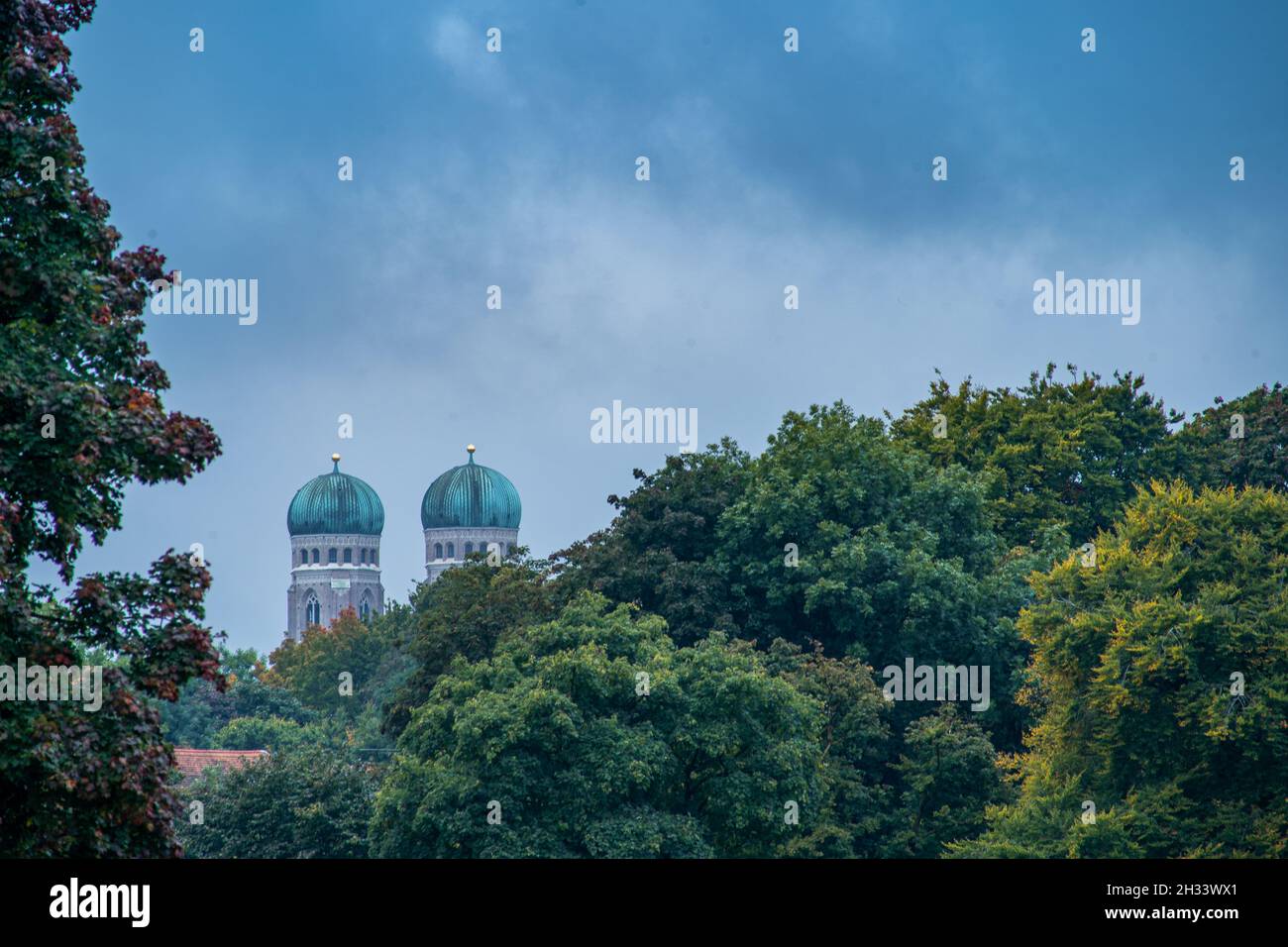 Ammira le cime delle due famose torri della Frauenkirche di Monaco, baviera, su cime degli alberi verdi e autunnali. Foto Stock