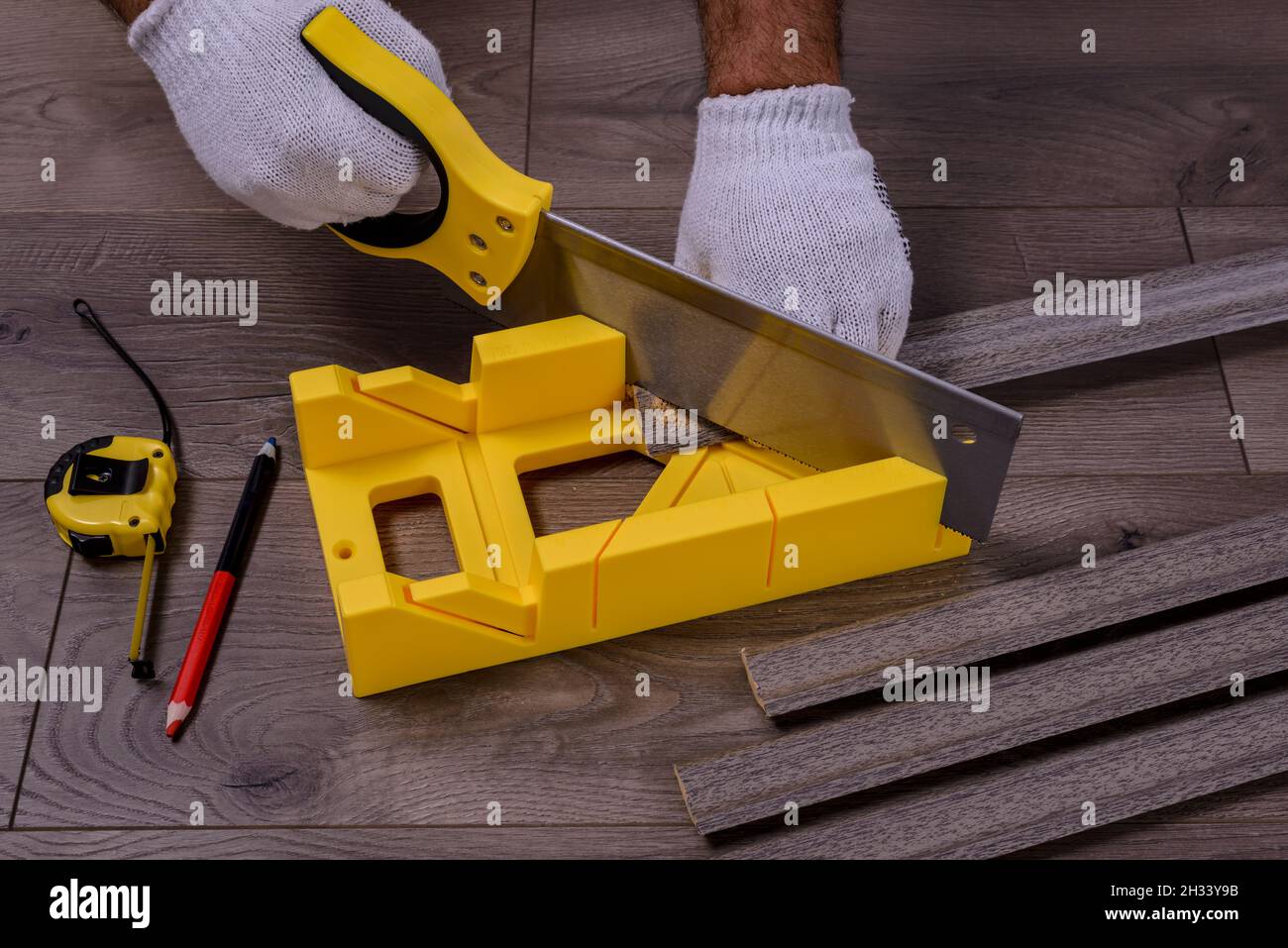 Un uomo taglia la tavola di battiscopa utilizzando una sega e una cassa di  taglio sul pavimento laminato Foto stock - Alamy