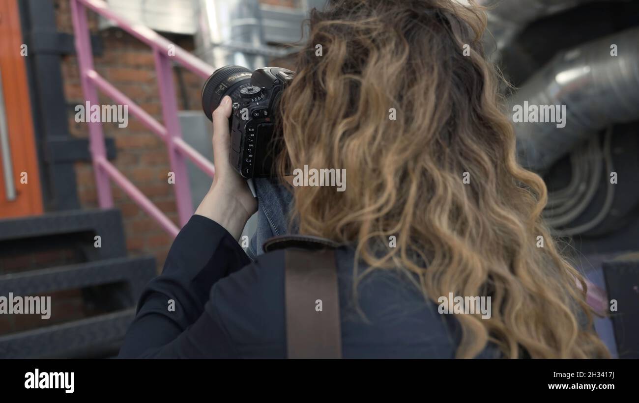 Vista posteriore del fotografo femminile durante le riprese fotografiche. Azione. Fotografo professionista femmina dà comandi e corregge i modelli durante le riprese fotografiche Foto Stock