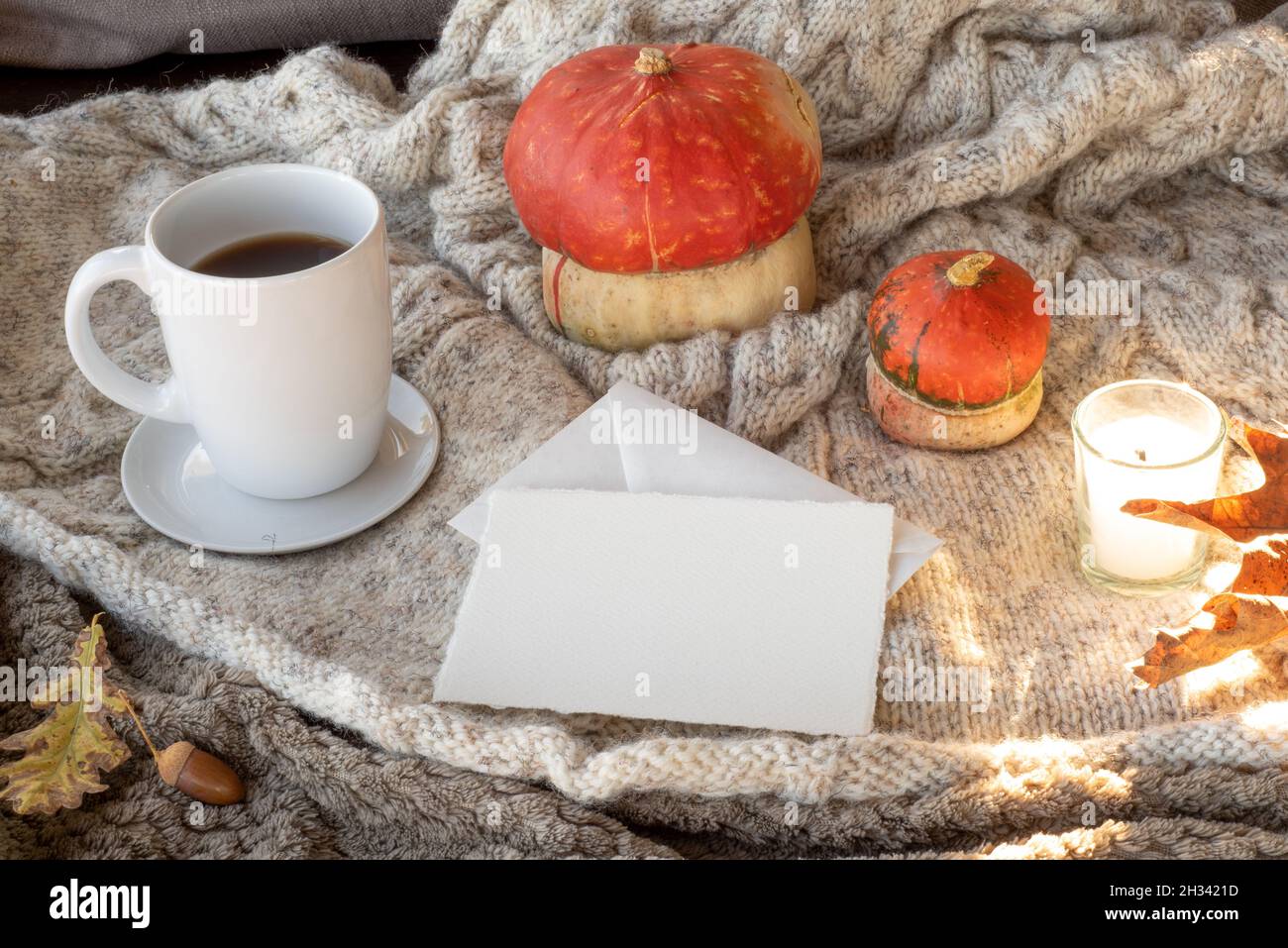 Accogliente sala colazione autunnale. Mockup biglietto di auguri vuoto e busta con tazza di caffè o tè, candela, zucche.Plaid lana background.fall, thanksgiv Foto Stock