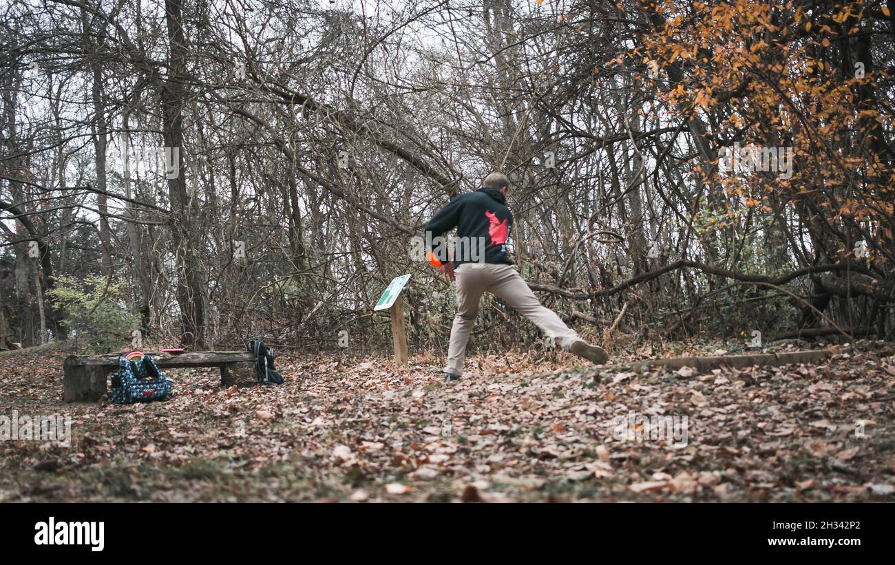 Giovane atletico che gioca a disc golf nei boschi durante l'inverno Foto Stock