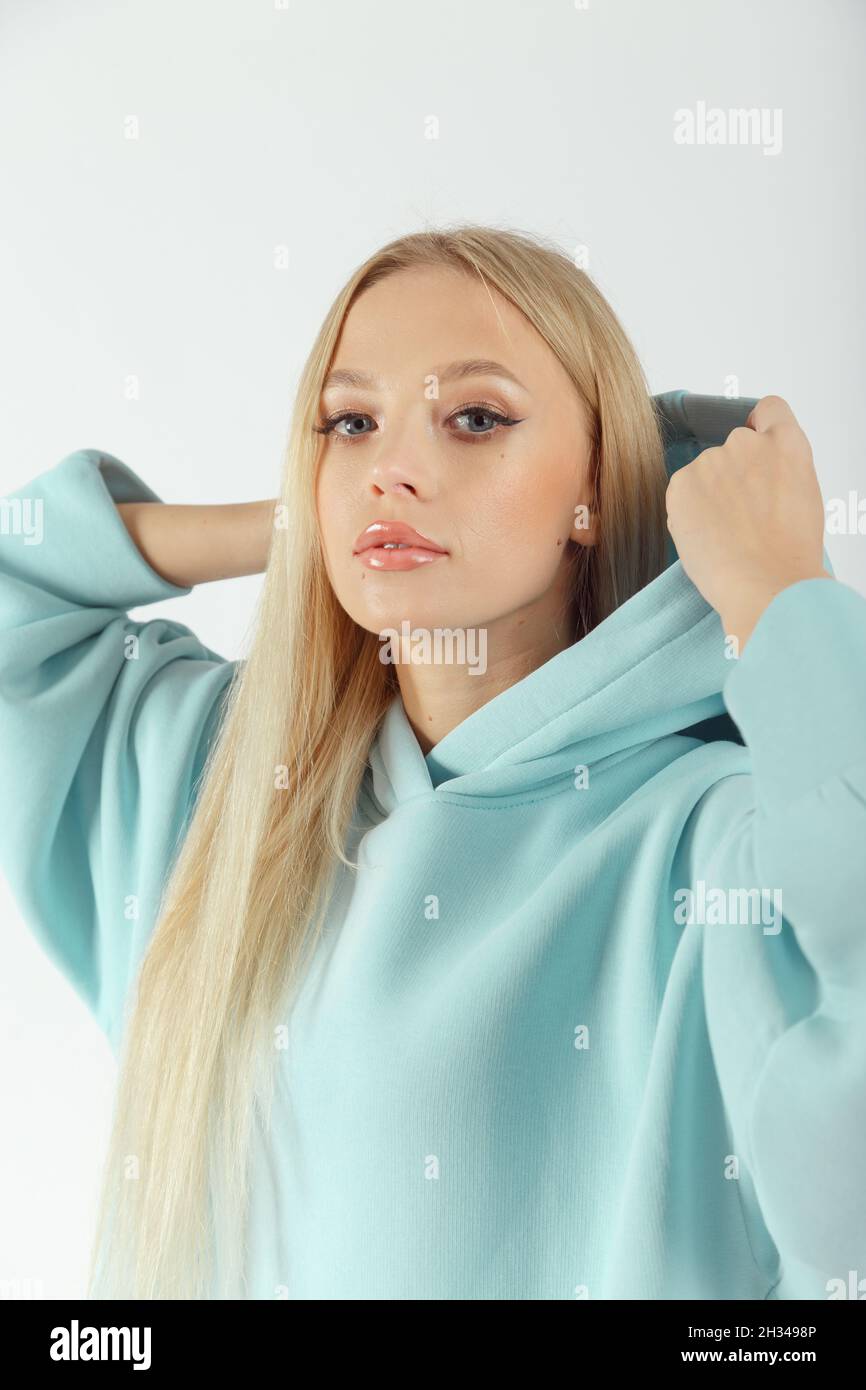 Giovane donna graziosa che indossa felpa con cappuccio turchese su sfondo bianco. Look sportivo femminile casual Foto Stock