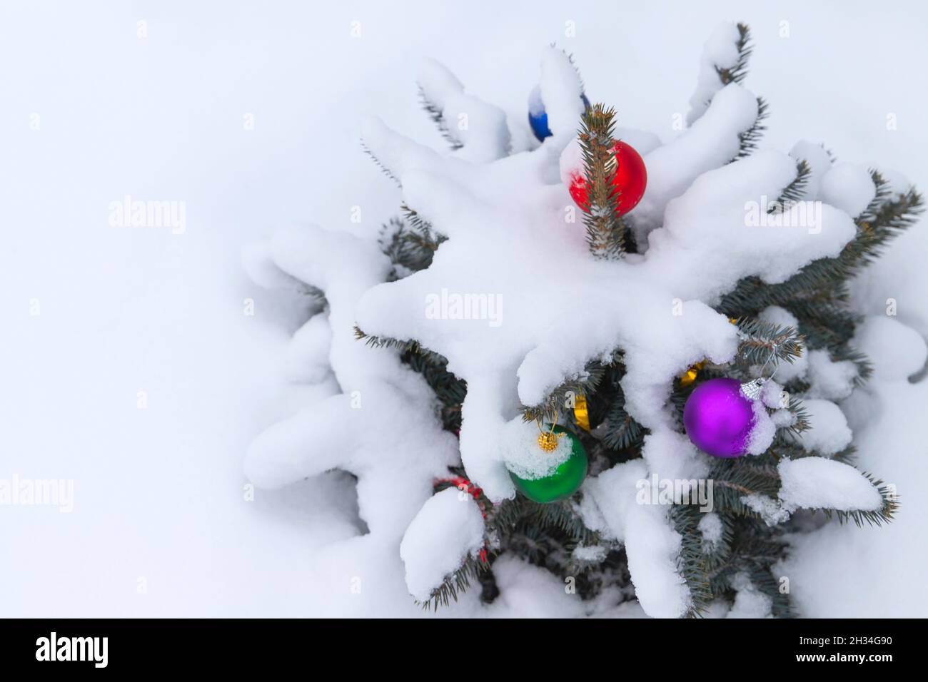 Piccolo albero di Natale coperto di neve con decorazioni colorate palle Foto Stock