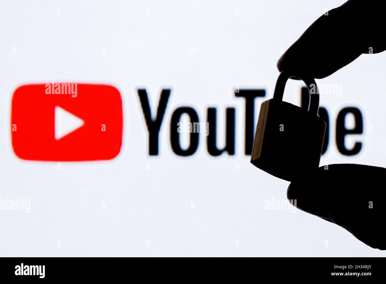 Le dita tengono un lucchetto di sicurezza chiuso sullo sfondo del logo della piattaforma di social media di YouTube. Il concetto di sicurezza dei dati in YouTube. Foto Stock