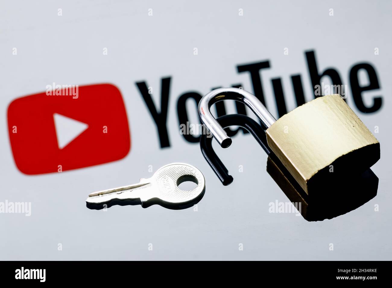 Un lucchetto di sicurezza aperto e una chiave sullo sfondo del logo della piattaforma di social media di YouTube nella riflessione speculare. Foto Stock