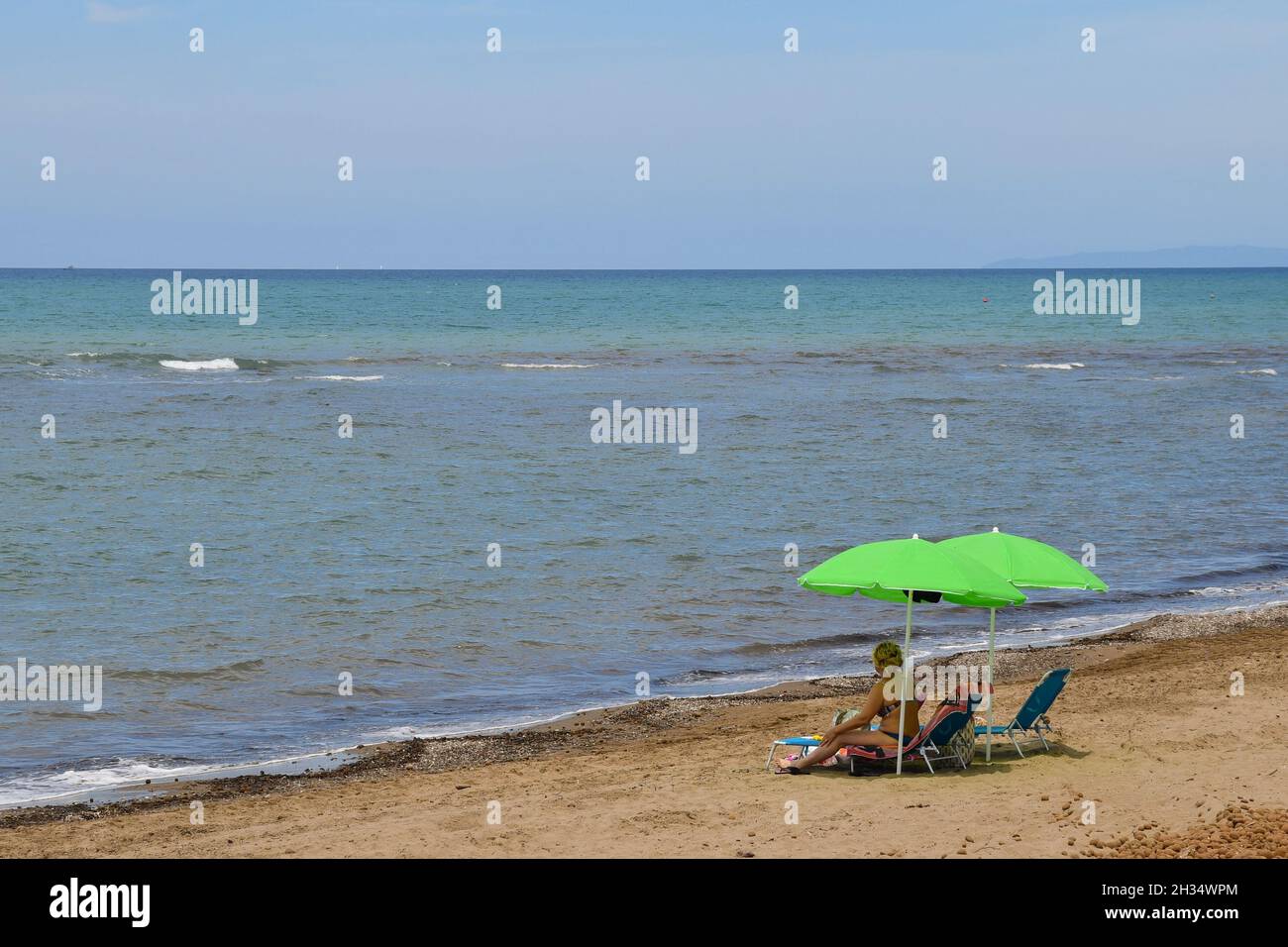 Spiaggia sabbiosa con una donna sotto gli ombrelloni sulla riva del mare della costa toscana in estate, San Vincenzo, Livorno, Toscana, Italia Foto Stock