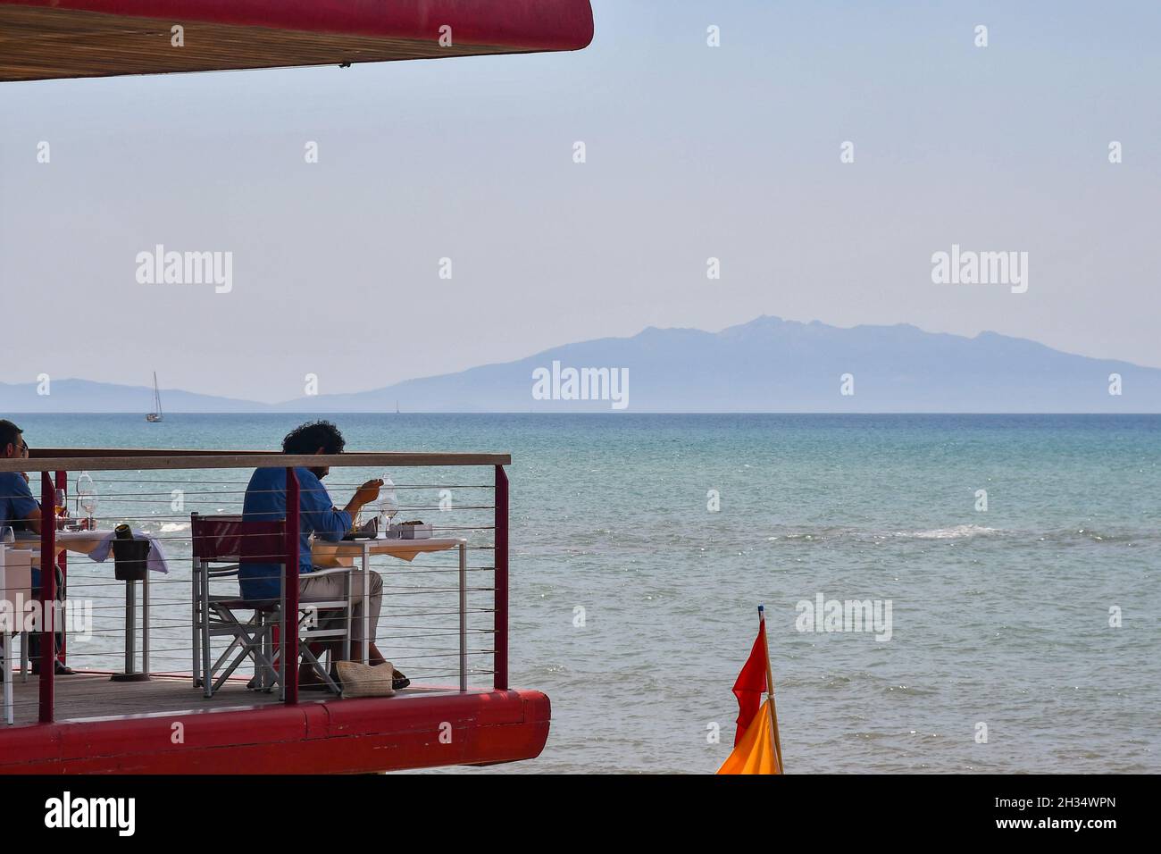 La gente ha pranzo sulla terrazza di un ristorante che si affaccia sul mare con la costa sullo sfondo in estate, San Vincenzo, Livorno, Toscana Foto Stock