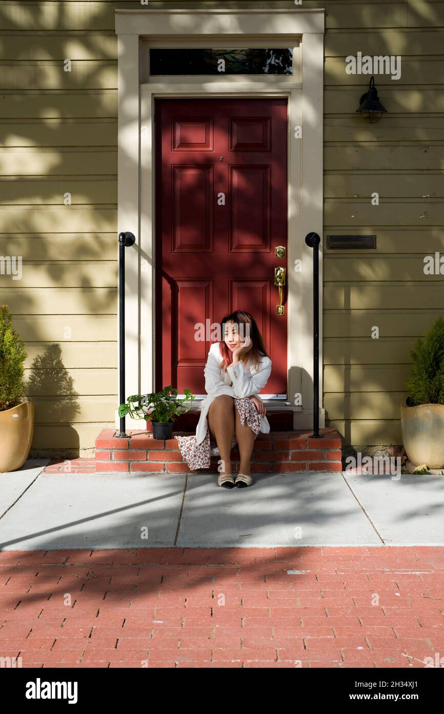 Giovane donna asiatica seduta guardando Casa pianta su un portico in attesa Foto Stock