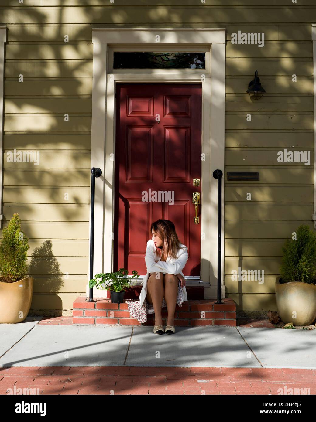 Giovane donna asiatica seduta guardando Casa pianta su un portico in attesa Foto Stock