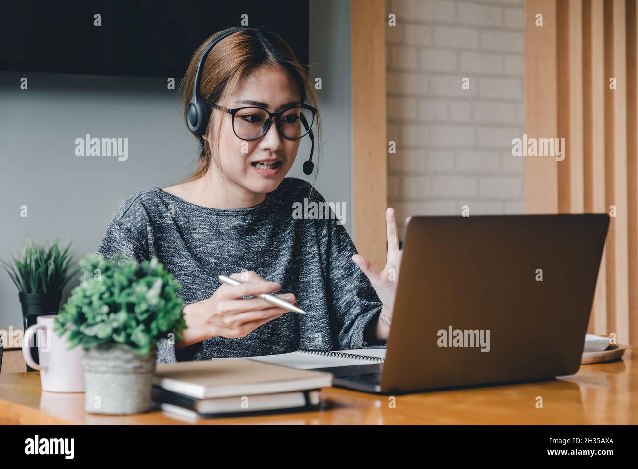 Donna asiatica indossare cuffie guardare il laptop godersi lo studio online con il tutor, ascoltare audio lezione guardare webinar preparare per gli esami, e-learn, auto Foto Stock