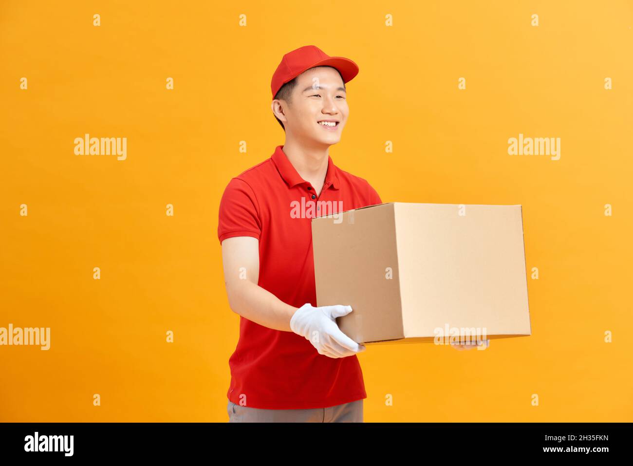 Immagine di un giovane uomo felice in berretto rosso in piedi con contenitore posta isolato su sfondo giallo. Foto Stock