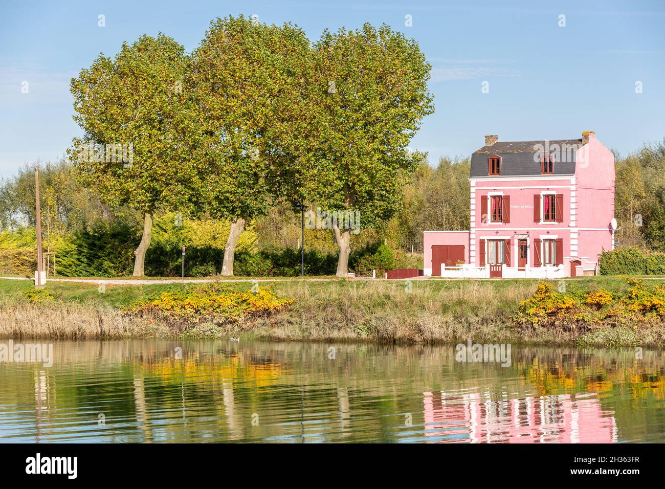 Casa rosa sul bordo del canale, riflessi sull'acqua. Saint-Valery, Baia della Somme, Francia Foto Stock