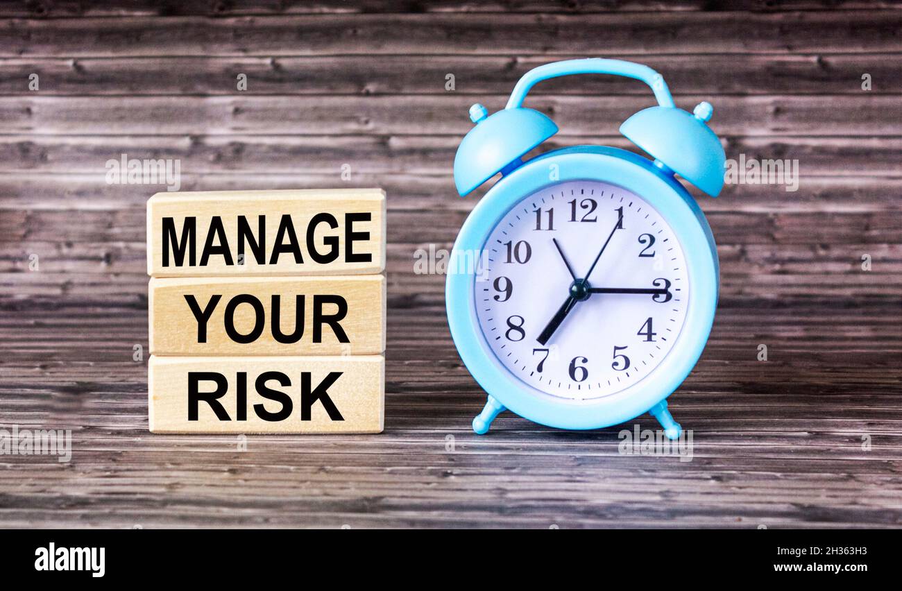 L'iscrizione GESTISCE I RISCHI su blocchi di costruzione, su un tavolo di legno con un orologio Foto Stock