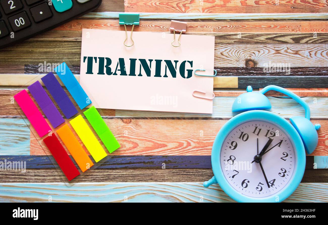 L'addestramento del testo è scritto su un taccuino, accanto agli adesivi, ad una calcolatrice e ad una sveglia su un tavolo di legno. Il concetto di apprendimento, competenze, pro Foto Stock