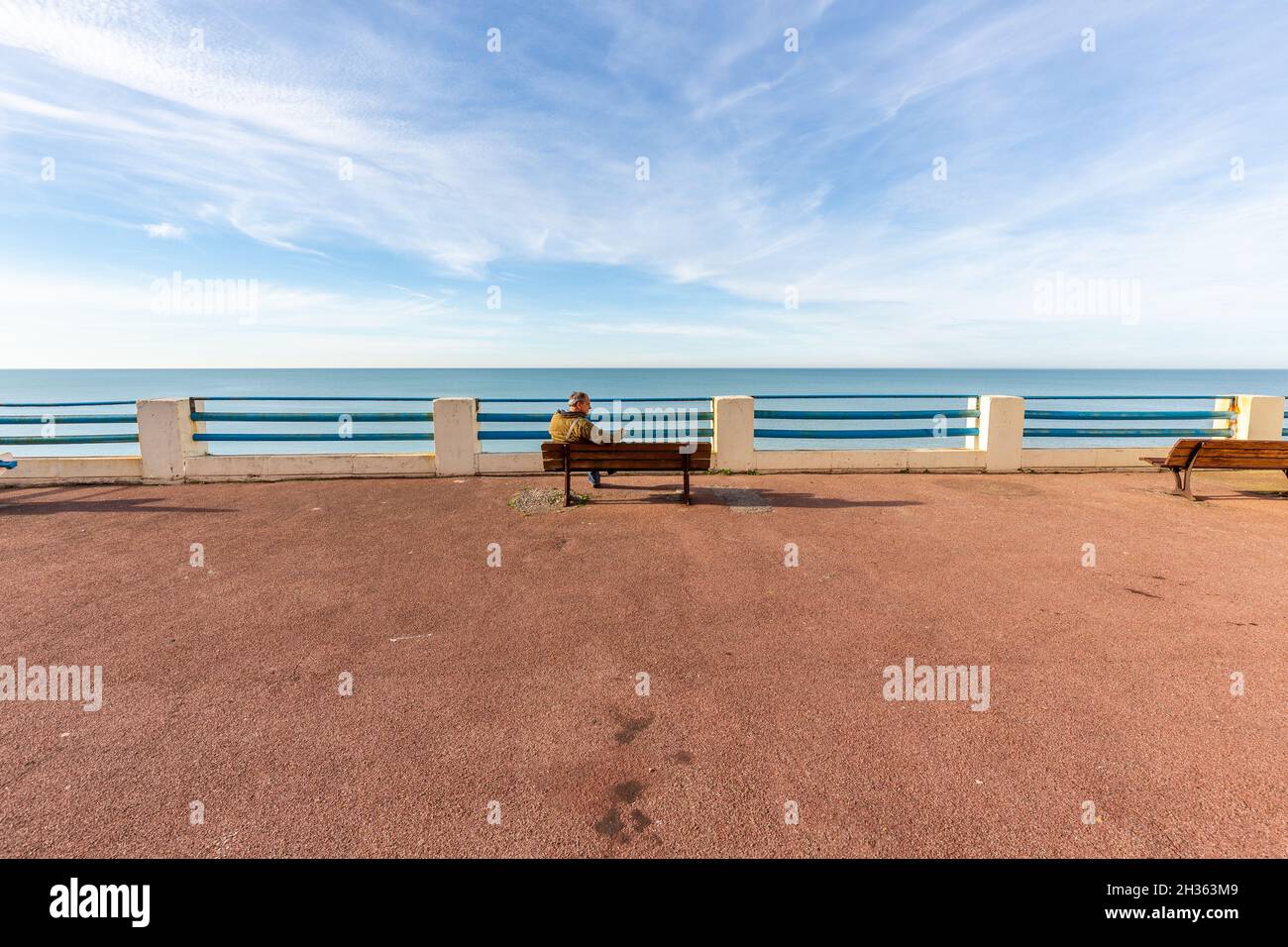 Uomo seduto su una panca su una terrazza con vista sul mare. Ault, Côte d'Opale, Francia Foto Stock