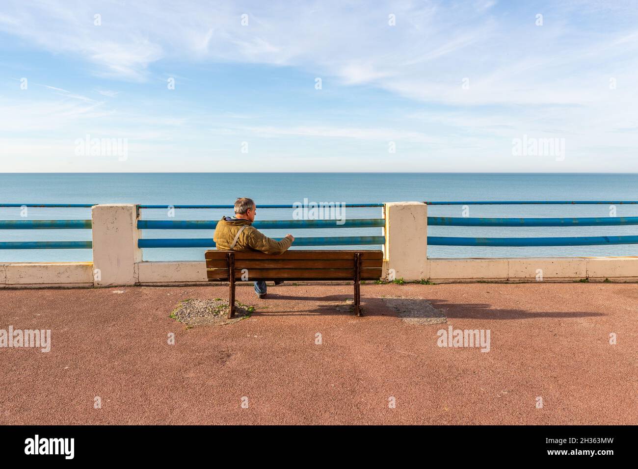 Uomo seduto su una panca su una terrazza con vista sul mare. Ault, Côte d'Opale, Francia Foto Stock