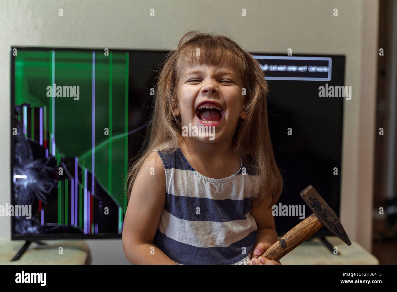 La bambina arrabbiata ha deliberatamente distrutto la TV con un martello ed è felice. Bambino incontrollabile con disturbi di condotta Foto Stock