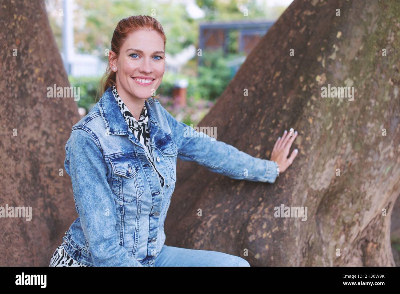 Felice giovane donna rossa caucasica che posa ad albero in parco in autunno Foto Stock