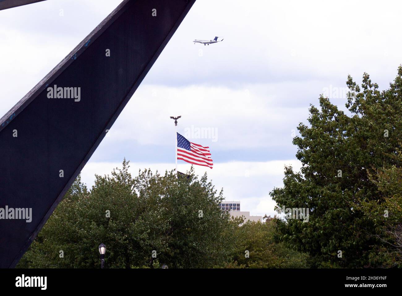 Una bandiera americana e un aeroplano visto attraverso l'Unisphere in Flushing Meadows Corona Park in Queens, New York City. Foto Stock