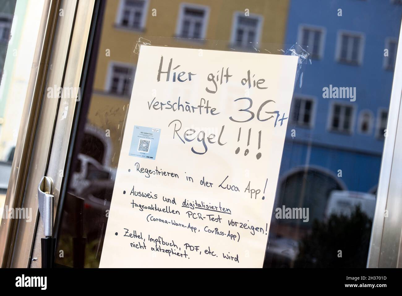 26 ottobre 2021, Baviera, Mühldorf am Inn: Un avviso su una finestra di un caffè si riferisce all'applicazione delle più severe 'regole 3G', mentre le case tipiche di Mühldorf nello stile Inn-Salzach si riflettono nella finestra. Mühldorf am Inn è attualmente una delle regioni bavaresi più colpite da Corona. Foto: Matthias Balk/dpa - ATTENZIONE: Il codice QR è stato parzialmente pixelato per motivi legali Foto Stock
