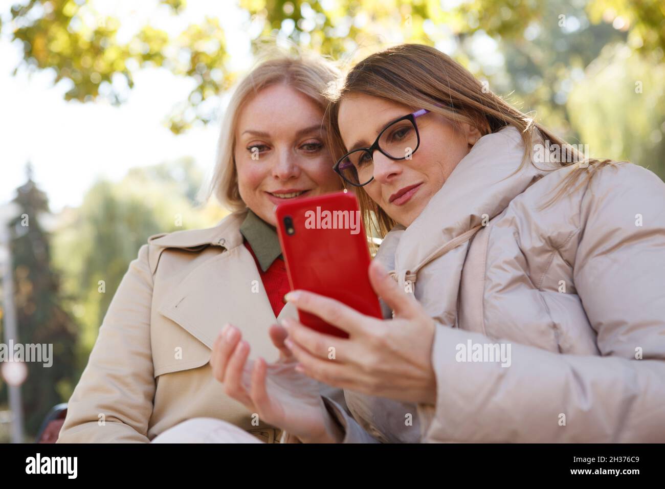 Inquadratura ad angolo basso di due donne mature che utilizzano lo smartphone nel parco Foto Stock
