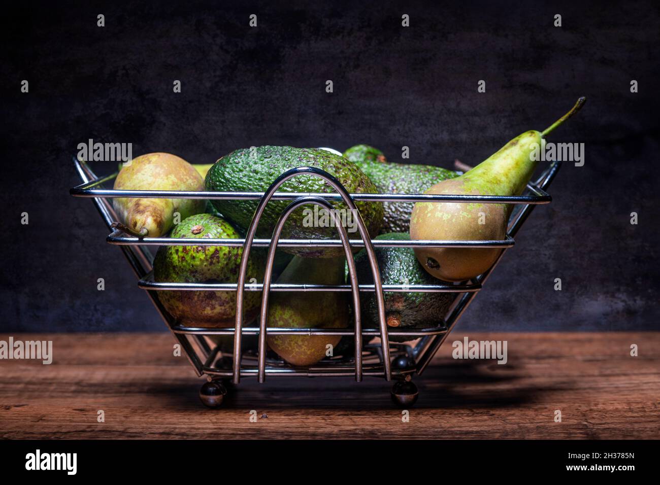 Pere e avocado in una ciotola di frutta d'acciaio, frutta verde e verdure. Foto Stock