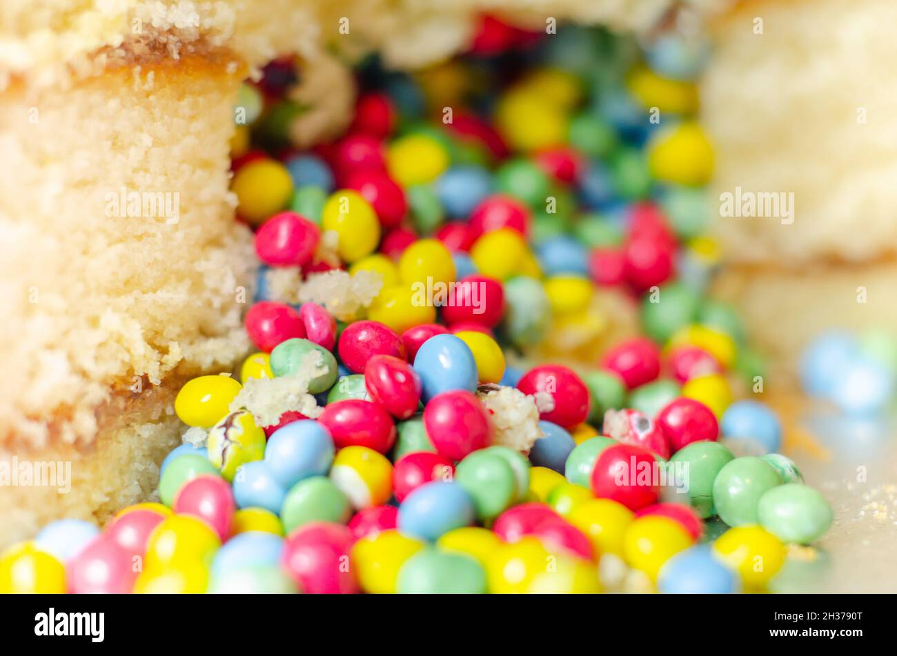 Spugna Madeira rivestita con glassa di colore giallo, stratificata con confettura di prugne e lamponi, ripiena e ricoperta di pennini di cioccolato multicolore e decorata Foto Stock