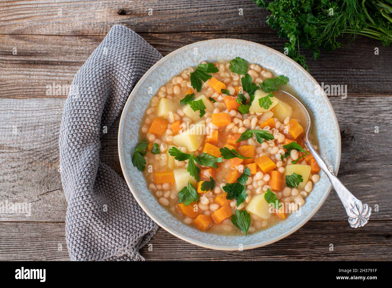 Zuppa di fagioli bianchi vegani con patate e verdure di radice isolate su tavola di legno con cucchiaio Foto Stock