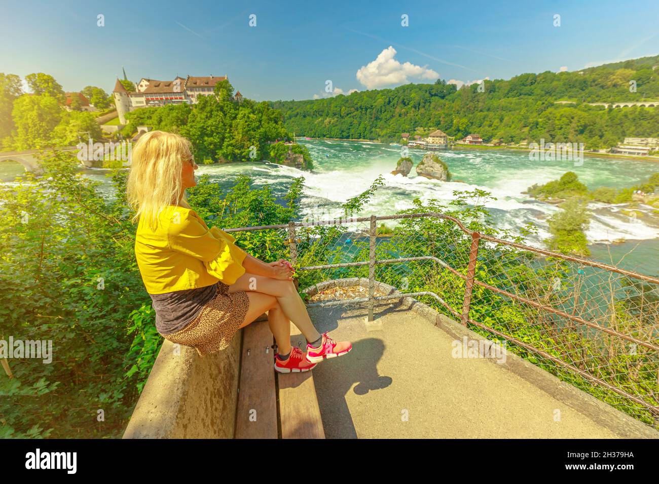 Ragazza elegante seduta sulla vista panoramica sulle Cascate del Reno in Svizzera. La cascata più grande d'Europa della Svizzera. 490 piedi di larghezza e 75 piedi di altezza Foto Stock
