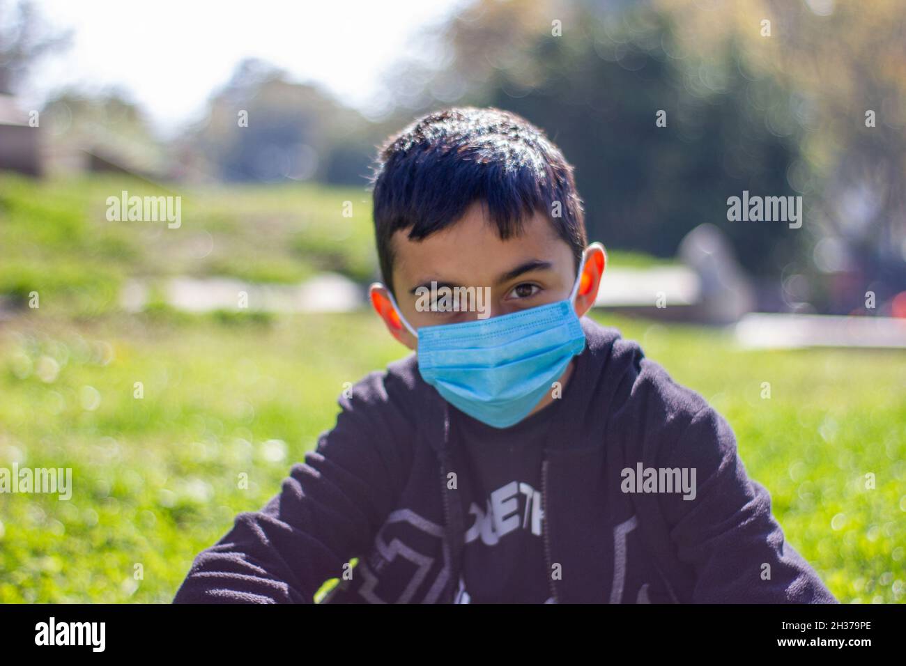 Vista frontale del ragazzo brunette in maschera blu e t-shirt nera. La nuova normalità dopo Covid-19. Messa a fuoco selettiva Foto Stock