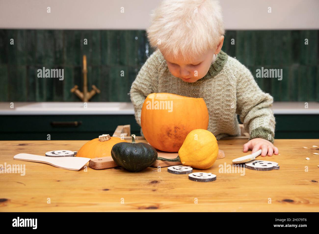 Un ragazzo giovane e carino che sbucciava in una zucca di Halloween mentre si fa una decorazione lanterna Foto Stock