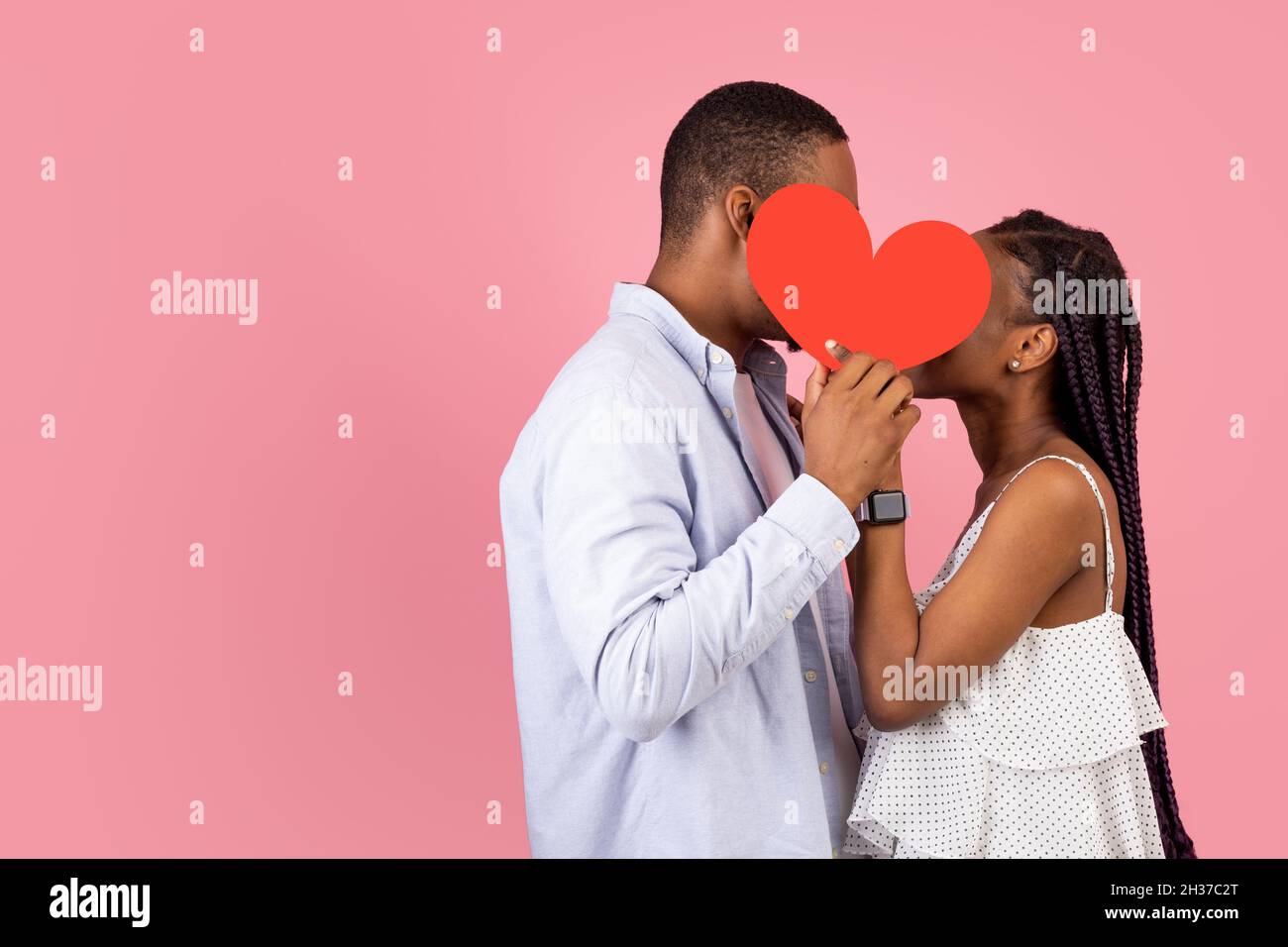 Giovane coppia Romantica nera Kissing Hiding dietro il cuore di carta rossa Foto Stock