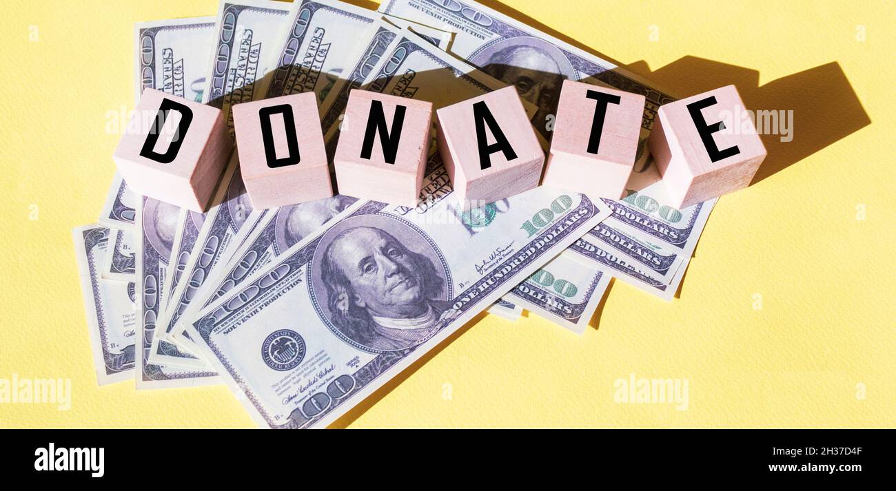 DONARE il testo su cubi di legno. Dollari giacciono su sfondo giallo Foto Stock