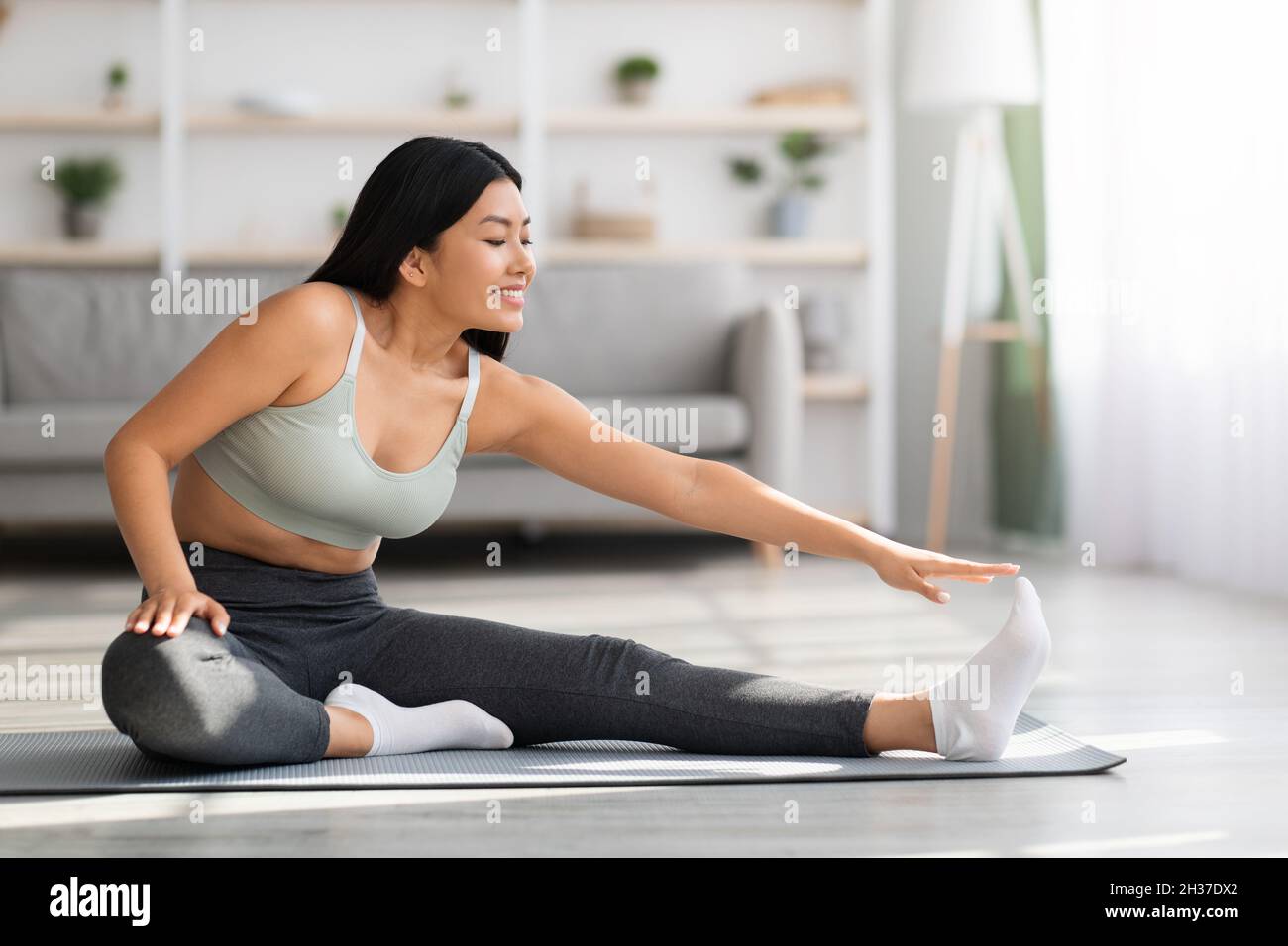 Sport giovane bella donna asiatica formazione a casa, stretching in soggiorno Foto Stock