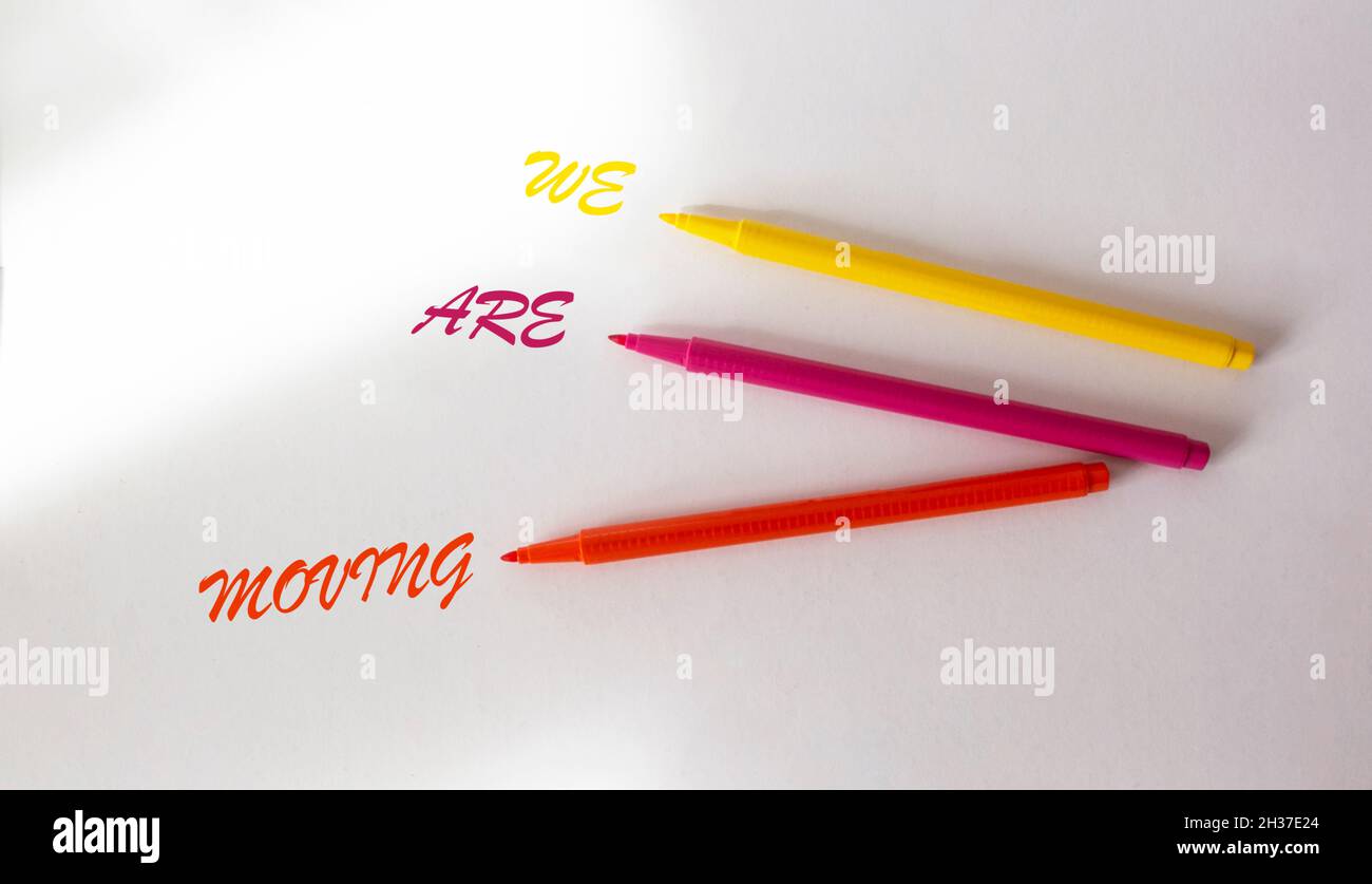 Testo ci stiamo muovendo scritto in pennarelli multicolore su uno sfondo bianco isolato. Foto Stock