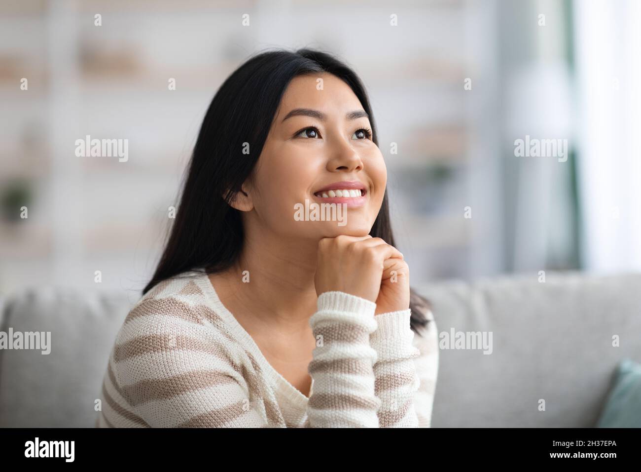 Ritratto di sognante giovane bella Asiatica Lady rilassante in interni domestici Foto Stock
