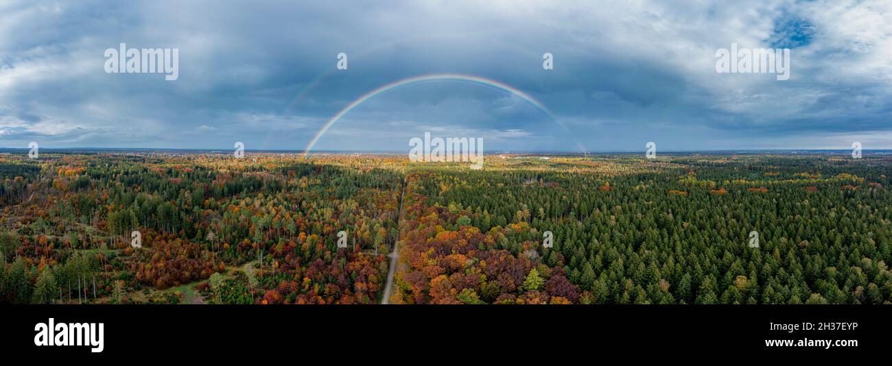 Panoramica arcobaleno doppio di una foresta colorata in autunno con la vista sullo skyline bavarese di Monaco sullo sfondo. Foto Stock