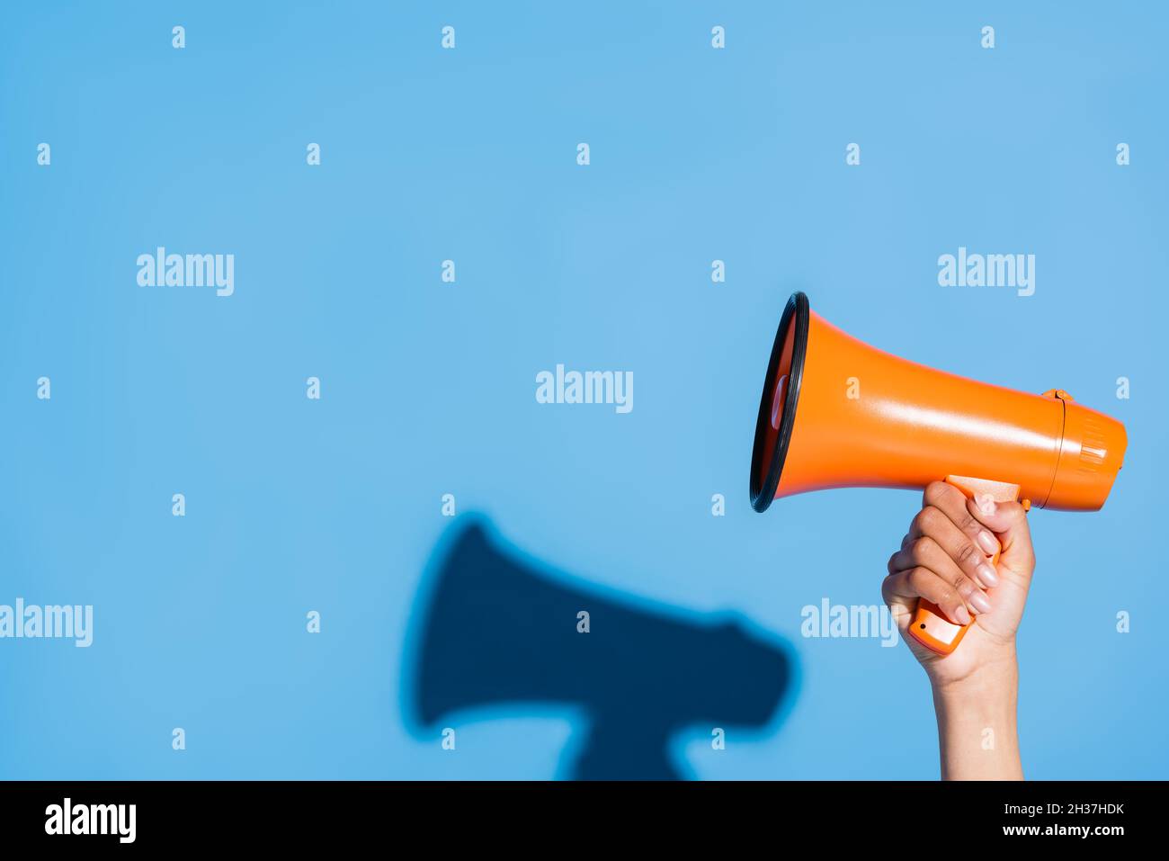 vista croppata della donna afroamericana che tiene il megaphone arancione su blu Foto Stock