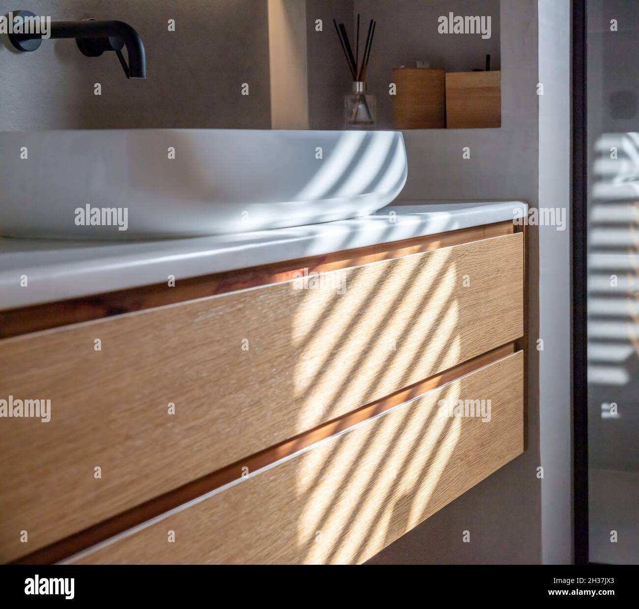 Lavandino in bagno su bancone in marmo bianco, rubinetti neri a parete, cassetto in legno e decorazioni. Interni dal design minimalista e moderno. Foto Stock