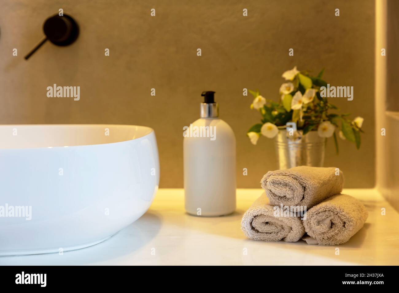 Rotoli di asciugamani da bagno, dispenser di sapone e lavandino bianco su un tavolo. Bagno moderno dettaglio interno. Foto Stock