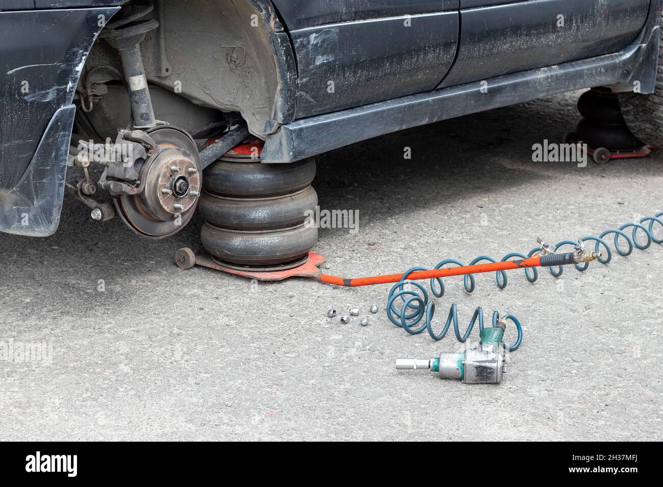 Sostituzione della ruota sul centro di assistenza pneumatici. Auto nera sporca senza una ruota sollevata sul martinetto pneumatico in un'officina di riparazione auto Foto Stock