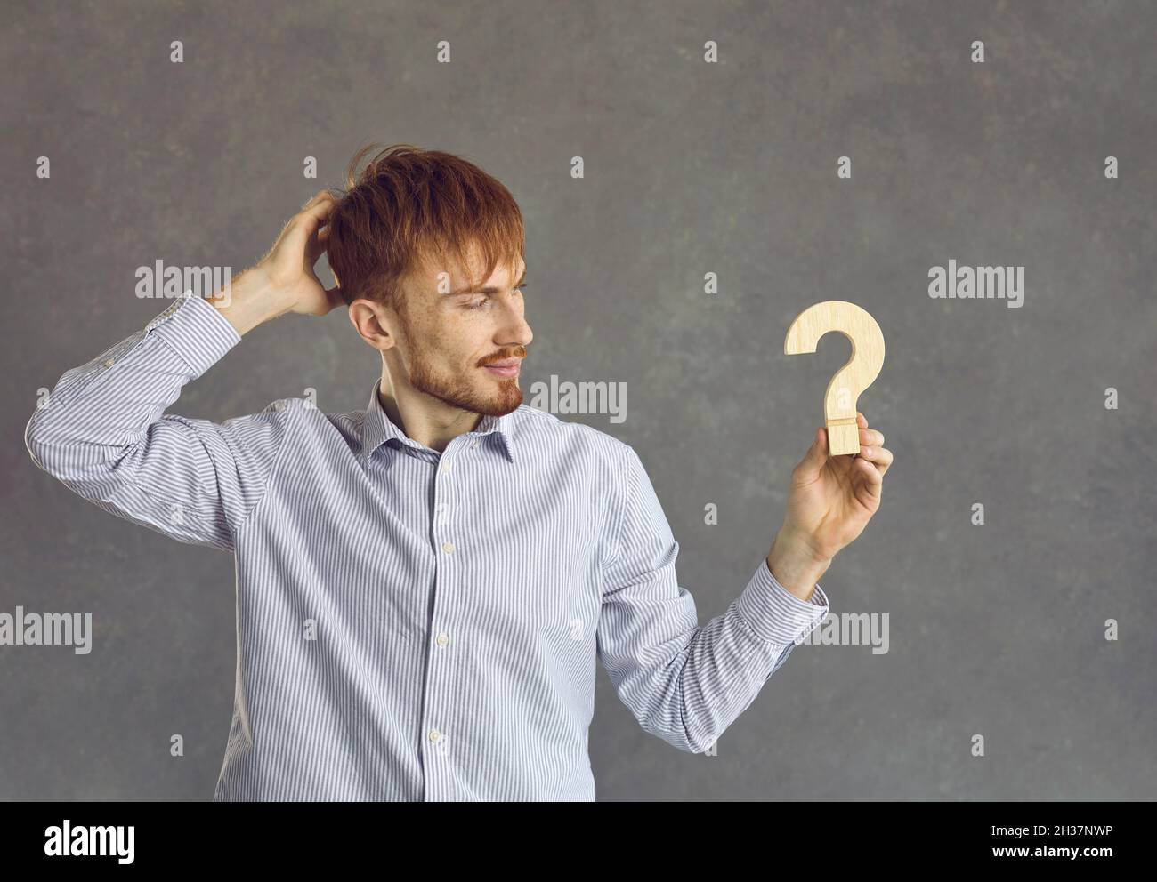 Uomo serio e premuroso che guarda la figura di domanda di legno in mano studio scatto Foto Stock