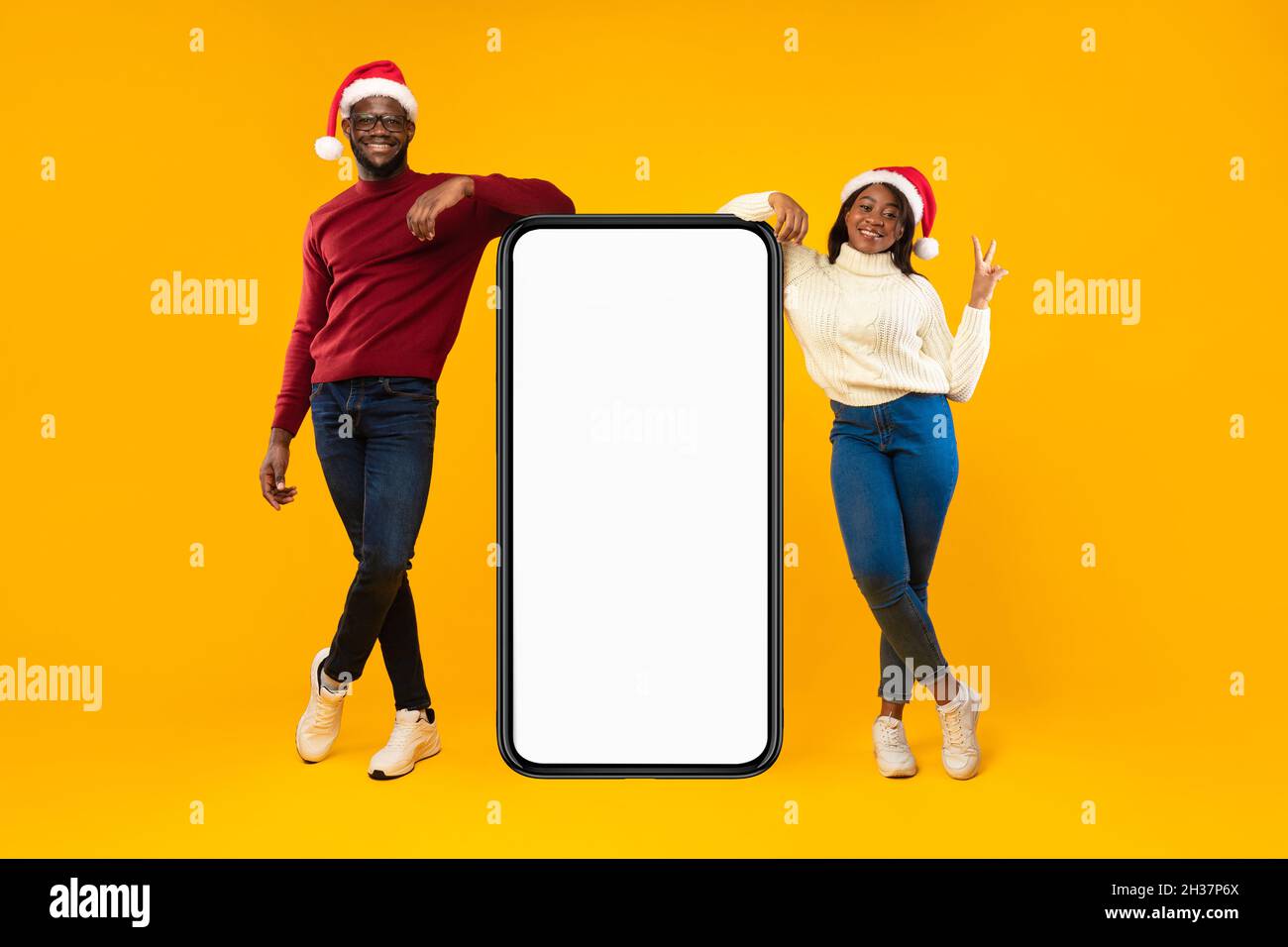 Coppia africana in piedi vicino al telefono schermo indossando cappelli di Santa, studio Foto Stock