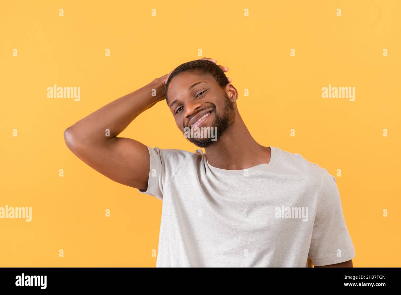 Ritratto di ragazzo afroamericano sorridendo alla macchina fotografica e toccando i capelli con la mano, posando su sfondo giallo Foto Stock