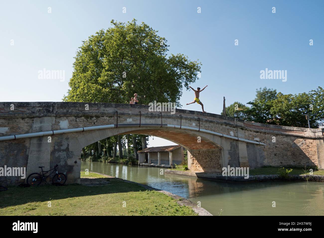 Gruppo di bambini francesi che nuotano nel Canal du Midi, regione dell'Occitanie, nel sud della Francia. Giovani amici che si divertono nel canale d'acqua e nel fiume in estate Foto Stock